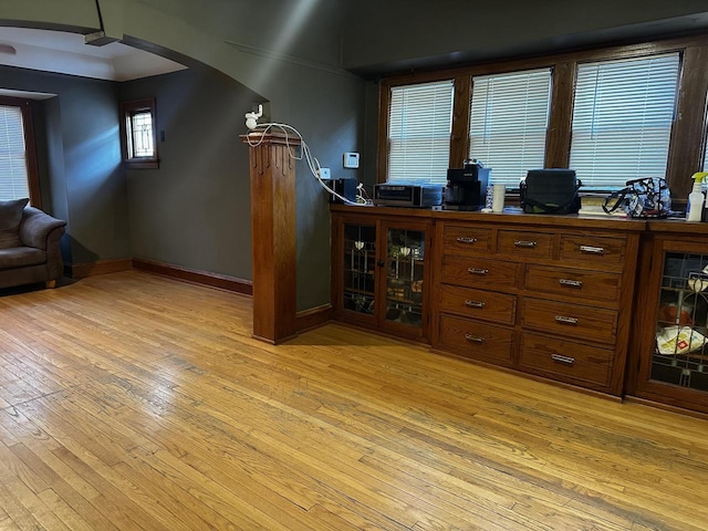 bar featuring arched walkways, light wood-style flooring, and baseboards