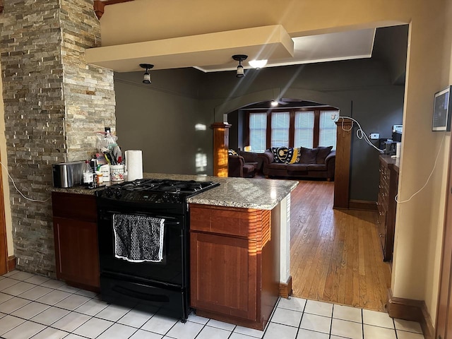 kitchen featuring light tile patterned floors, brown cabinetry, open floor plan, black range with gas cooktop, and light stone countertops