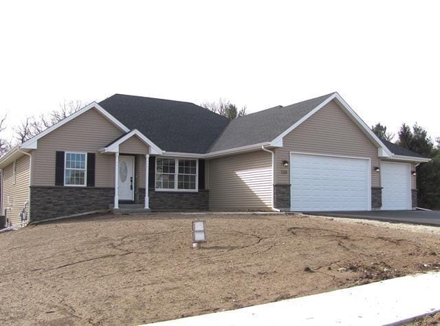 single story home featuring a garage, driveway, stone siding, and central air condition unit