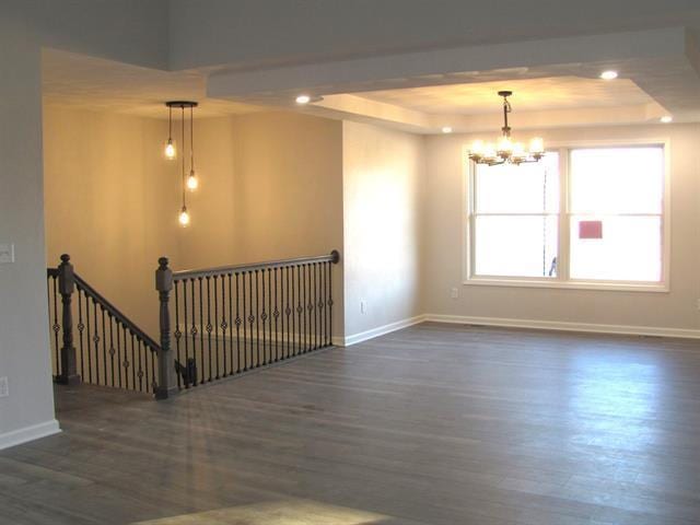 empty room with a notable chandelier, baseboards, a raised ceiling, and dark wood-type flooring