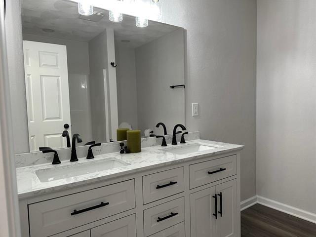 bathroom with double vanity, wood finished floors, a sink, and baseboards