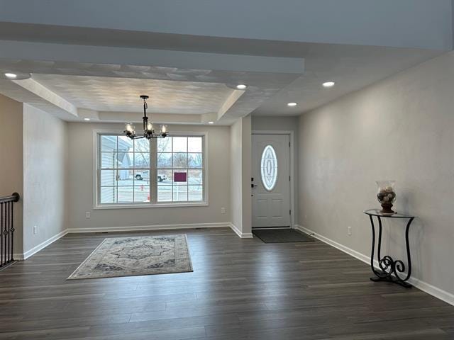 entryway featuring baseboards, dark wood-type flooring, a raised ceiling, and an inviting chandelier