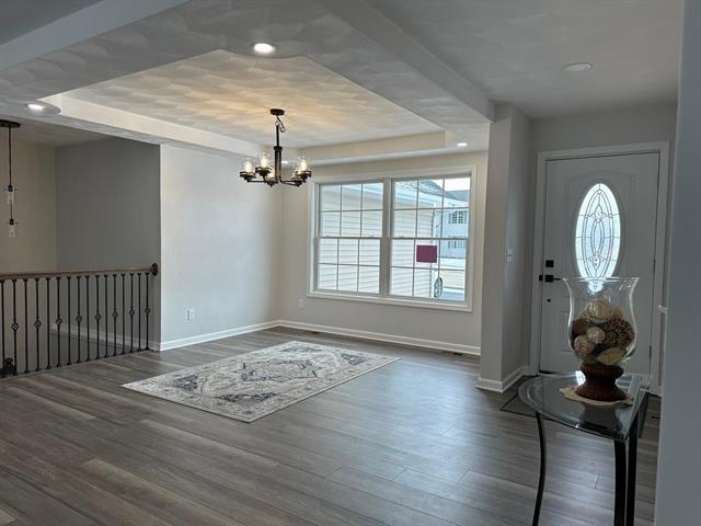 foyer featuring a tray ceiling, dark wood finished floors, baseboards, and an inviting chandelier