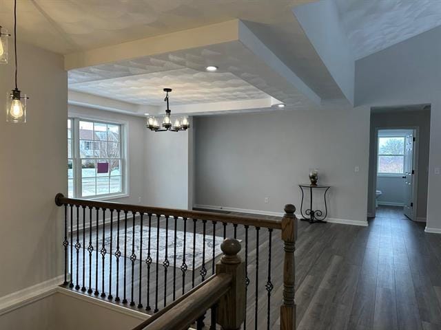 hallway featuring baseboards, dark wood-type flooring, a tray ceiling, an upstairs landing, and a chandelier