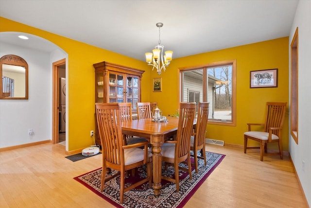 dining room with arched walkways, baseboards, visible vents, and light wood-style floors