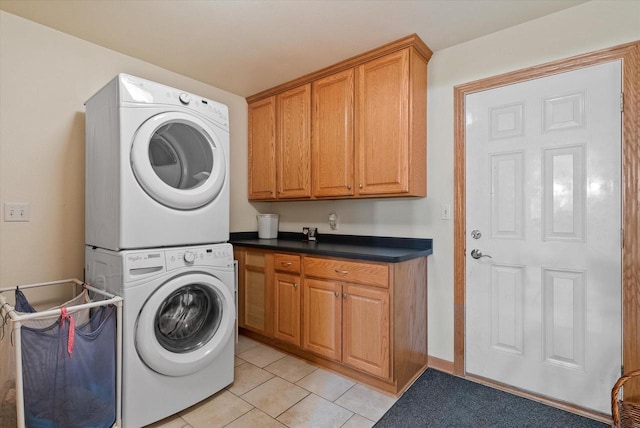 laundry area featuring light tile patterned floors, stacked washing maching and dryer, and cabinet space