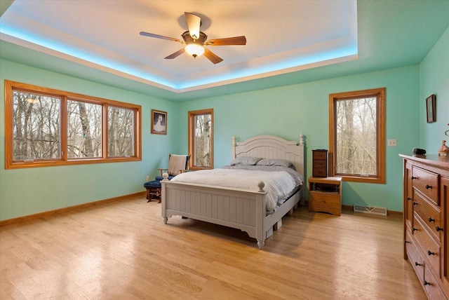 bedroom featuring light wood-style flooring, a raised ceiling, and visible vents