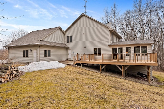 rear view of property with a shingled roof, a chimney, a deck, and a lawn