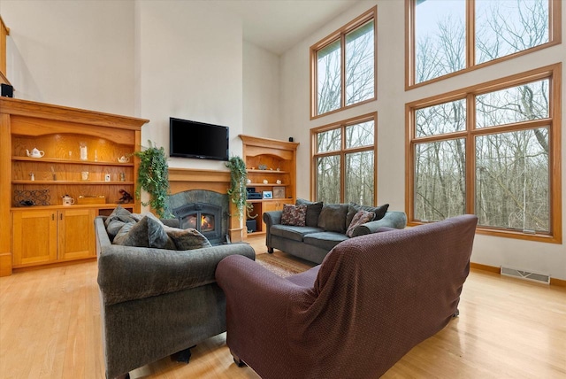 living room featuring a lit fireplace, light wood-style flooring, a towering ceiling, and visible vents