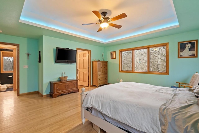 bedroom featuring a raised ceiling, ceiling fan, light wood-style flooring, and baseboards