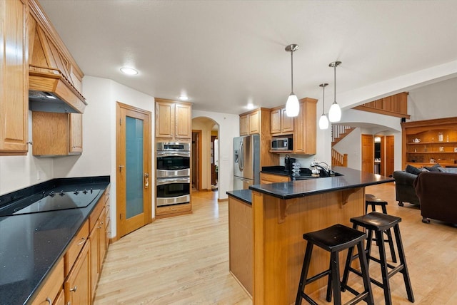 kitchen featuring light wood-style flooring, appliances with stainless steel finishes, arched walkways, and a kitchen breakfast bar