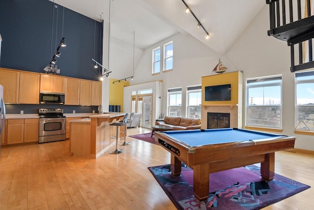 playroom with billiards, a towering ceiling, light wood finished floors, a glass covered fireplace, and track lighting