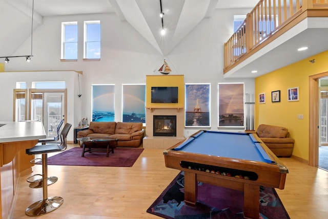 recreation room with light wood-type flooring, a tile fireplace, a towering ceiling, and baseboards