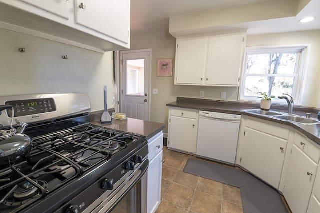 kitchen featuring stainless steel gas range oven, dishwasher, dark countertops, white cabinetry, and a sink