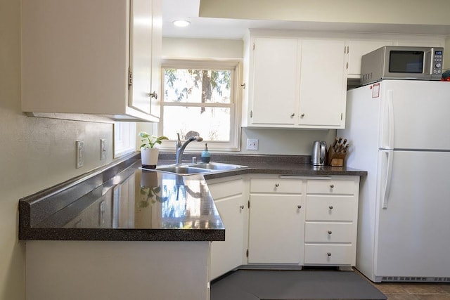 kitchen featuring dark countertops, stainless steel microwave, freestanding refrigerator, white cabinetry, and a sink