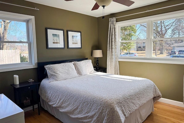 bedroom featuring ceiling fan, multiple windows, wood finished floors, and baseboards