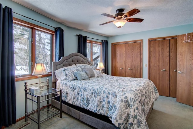 carpeted bedroom with a ceiling fan, a textured ceiling, visible vents, and multiple closets