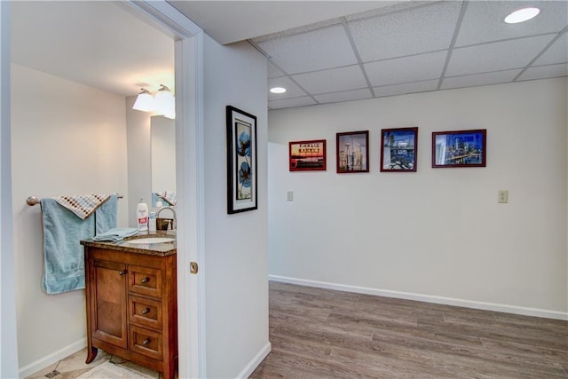 bathroom with a paneled ceiling, recessed lighting, wood finished floors, vanity, and baseboards