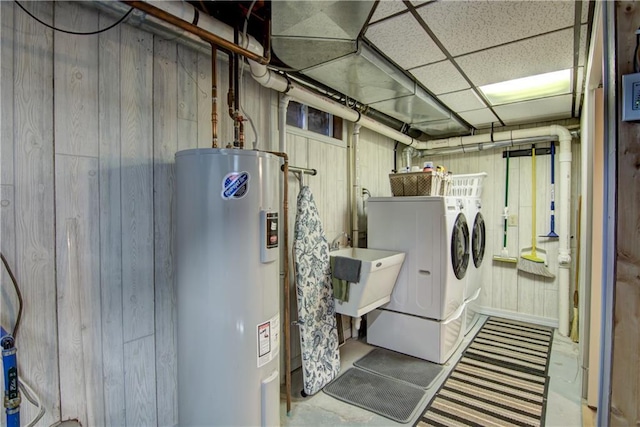 clothes washing area with laundry area, wooden walls, electric water heater, washer and dryer, and a sink