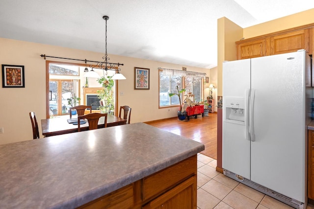 kitchen with a wealth of natural light, white refrigerator with ice dispenser, light tile patterned flooring, and dark countertops