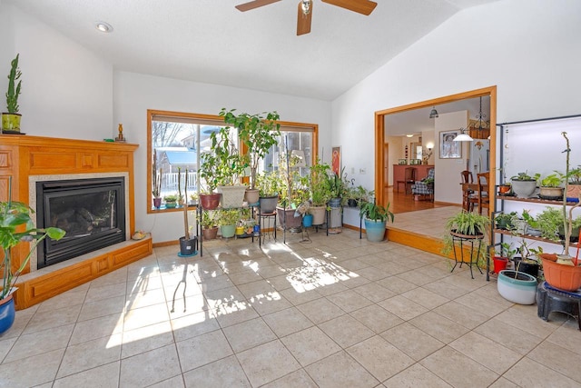 living room with light tile patterned floors, ceiling fan, baseboards, vaulted ceiling, and a glass covered fireplace