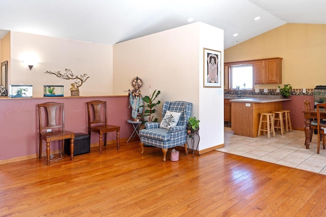 living area with baseboards, vaulted ceiling, and light wood finished floors