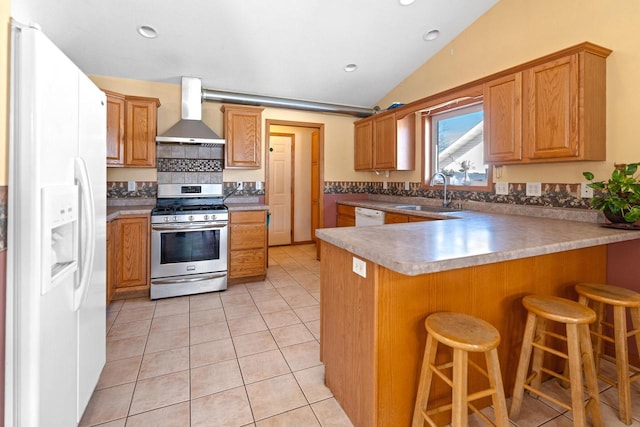 kitchen with light tile patterned floors, a peninsula, white appliances, a sink, and wall chimney exhaust hood