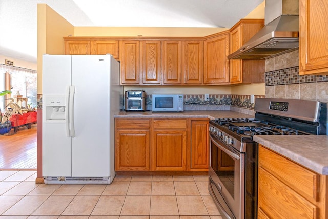 kitchen featuring light tile patterned floors, white appliances, wall chimney range hood, decorative backsplash, and brown cabinetry