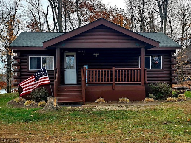 cabin featuring covered porch, a shingled roof, log exterior, and a front yard