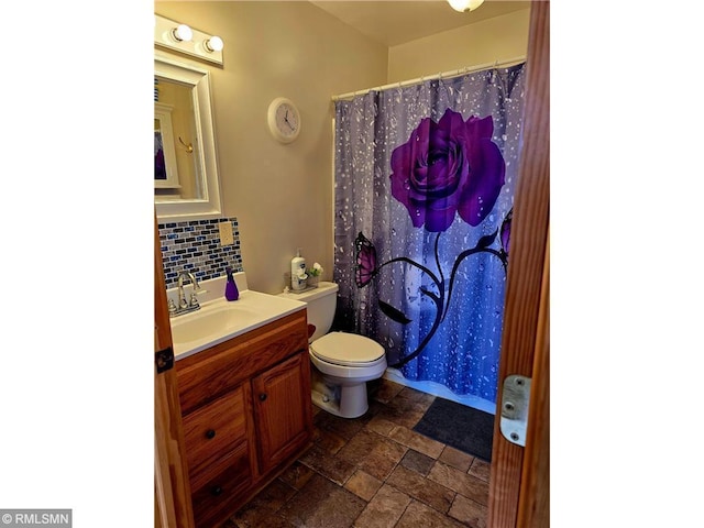 bathroom featuring stone tile floors, tasteful backsplash, a shower with shower curtain, toilet, and vanity