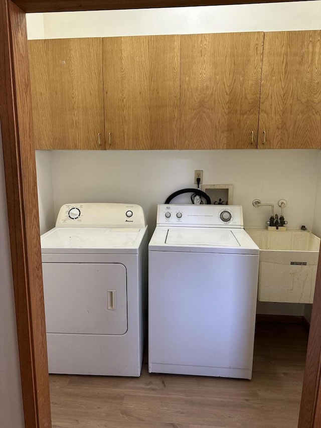 washroom featuring cabinet space, a sink, light wood finished floors, and separate washer and dryer