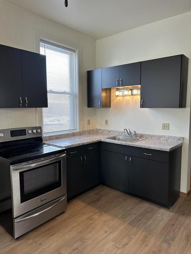 kitchen with light countertops, light wood-style floors, stainless steel range with electric cooktop, a sink, and dark cabinets