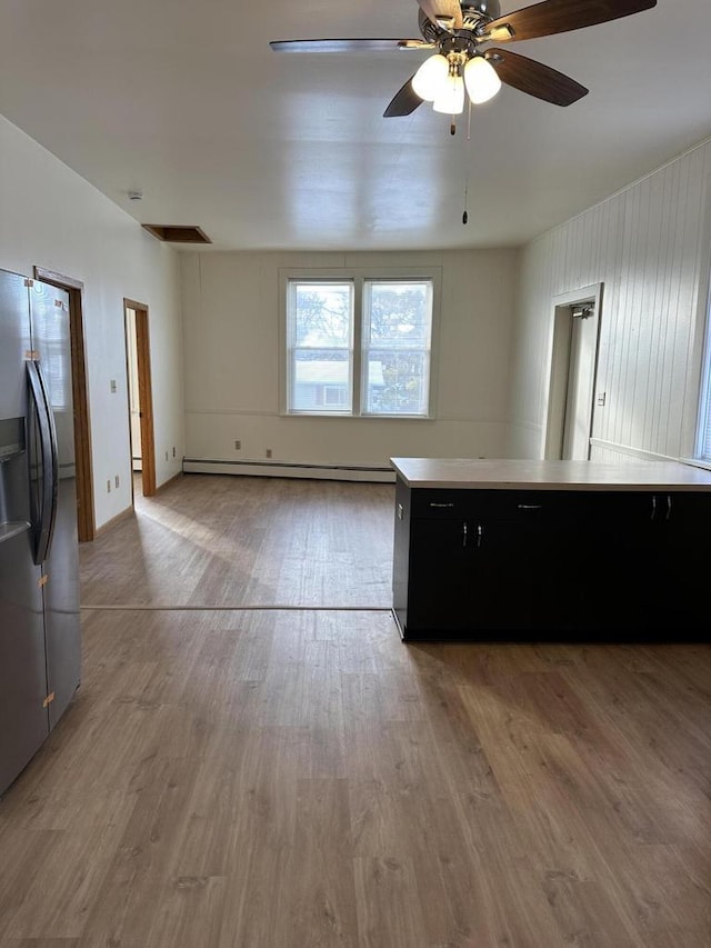 kitchen with stainless steel fridge, a baseboard radiator, dark cabinets, wood finished floors, and light countertops