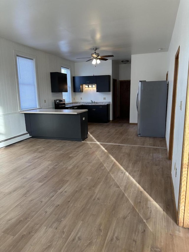 kitchen with light countertops, freestanding refrigerator, wood finished floors, dark cabinetry, and a peninsula