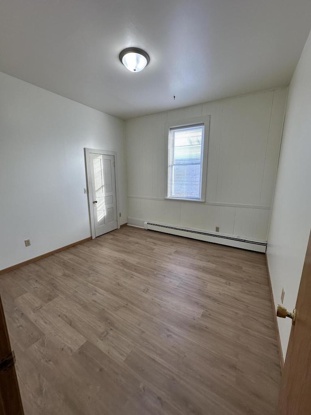 unfurnished room featuring baseboards, baseboard heating, and light wood-style floors