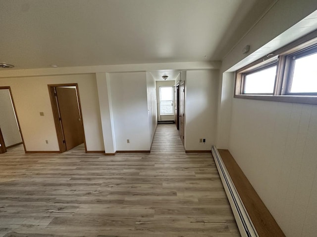 spare room with a baseboard radiator, baseboards, plenty of natural light, and light wood finished floors