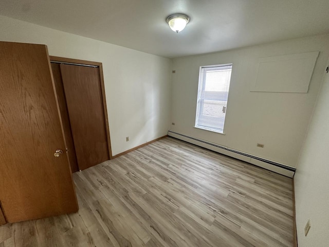 unfurnished bedroom with light wood-style floors, baseboards, a baseboard heating unit, and a closet