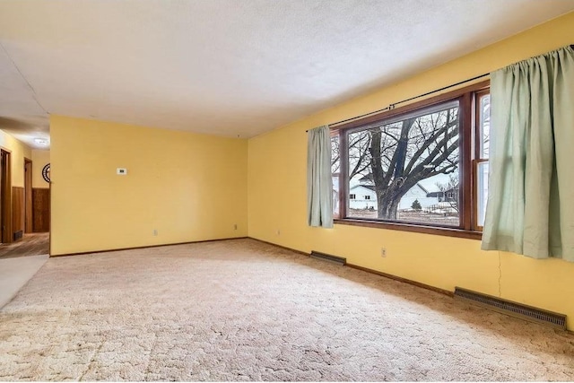 spare room featuring a textured ceiling, carpet, visible vents, and baseboards