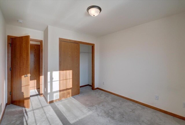 unfurnished bedroom with baseboards, a closet, and light colored carpet