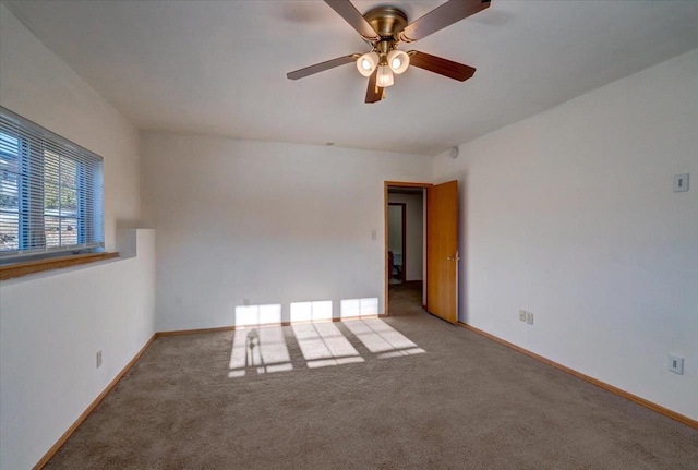 carpeted spare room featuring a ceiling fan and baseboards