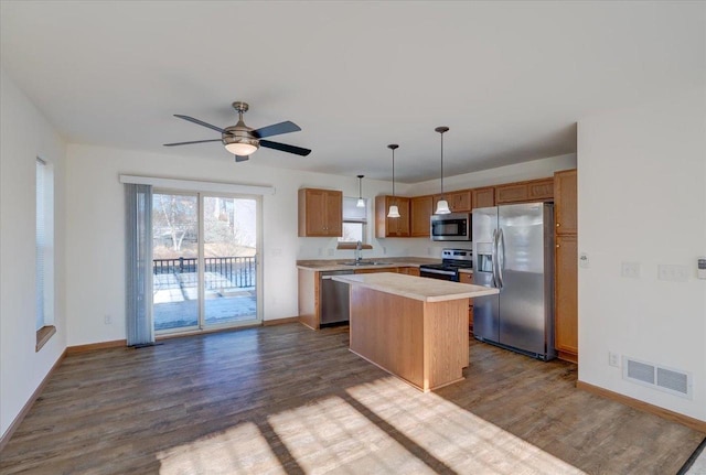 kitchen with stainless steel appliances, light countertops, visible vents, a kitchen island, and a sink