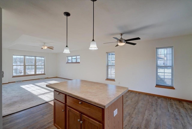 kitchen featuring a kitchen island, open floor plan, light countertops, brown cabinetry, and decorative light fixtures