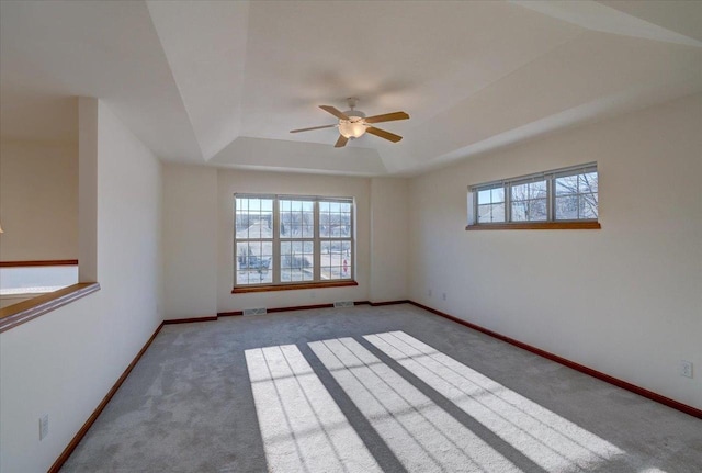 carpeted spare room featuring ceiling fan, a tray ceiling, visible vents, and baseboards