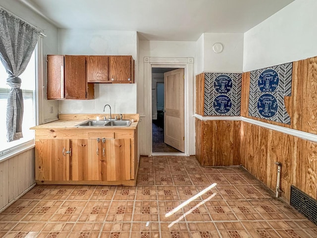 kitchen featuring light countertops, visible vents, brown cabinetry, wood walls, and a sink