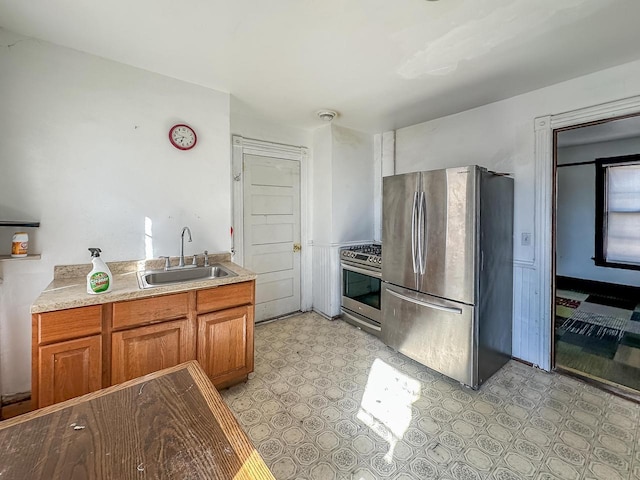 kitchen with a sink, light countertops, appliances with stainless steel finishes, brown cabinets, and light floors