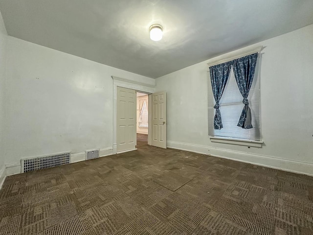 spare room with dark carpet, visible vents, and baseboards