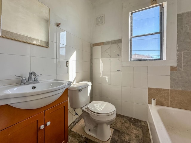 bathroom featuring a tub to relax in, toilet, visible vents, vanity, and tile walls