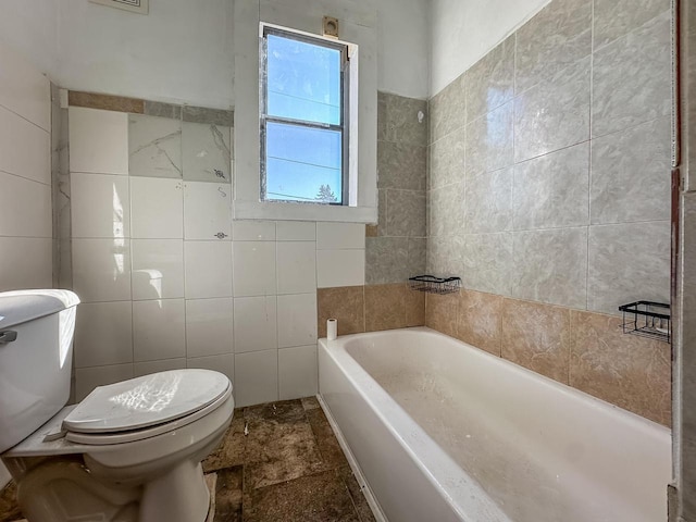 bathroom featuring toilet, a garden tub, and tile walls