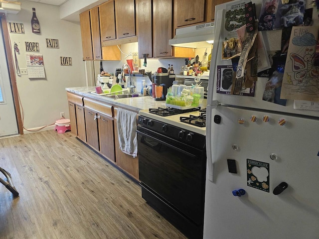 kitchen with black gas range oven, freestanding refrigerator, light countertops, light wood-type flooring, and under cabinet range hood