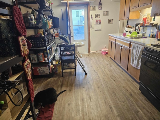 kitchen with black range with gas cooktop, a sink, light countertops, light wood-type flooring, and brown cabinets